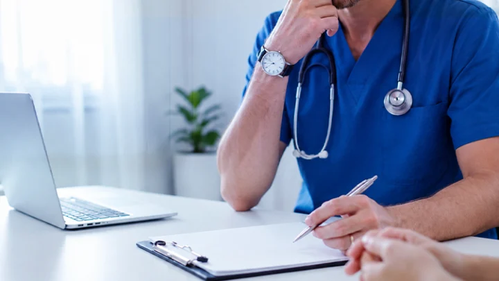 Doctor in blue scrubs taking notes on a clipboard during a consultation